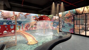 Un espacio de juegos interior con tobogán, fuentes de agua y un mural con vida marina.