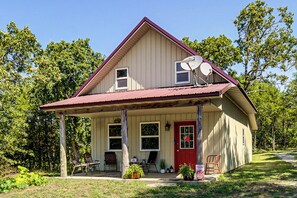 Ein zweistöckiges Haus mit roter Tür, einer überdachten Veranda und Satellitenschüsseln auf dem Dach.