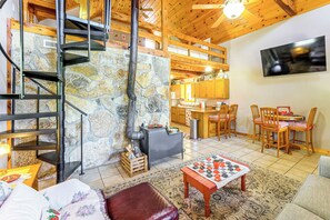 A cozy interior with a stone wall, a wooden staircase, a dining area with a checkered table, and a kitchen with wooden cabinets. - Ozarks Escape! Farmhouse w/ Fire Pit + Trails (Aurora)