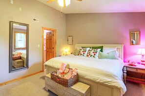 A bedroom with a large bed, a nightstand, a mirror, a door, and a small wooden chest. - Ozarks Escape! Farmhouse w/ Fire Pit + Trails (Aurora)