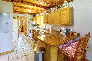 Eine Küche mit Holzausbau, einem Edelstahl-Mülleimer, einem karierten Stuhl und einem gefliesten Boden.