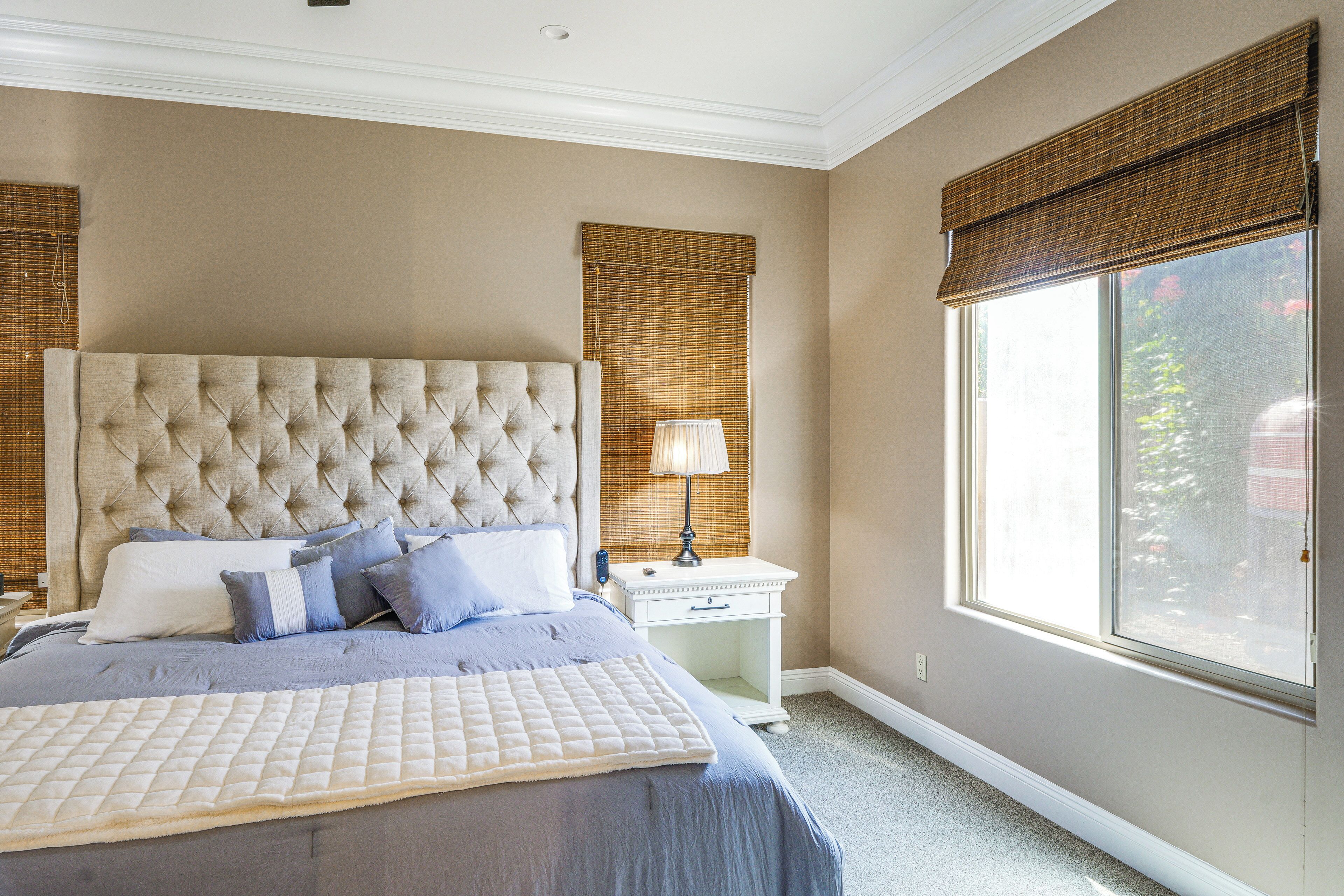 A bedroom with a large bed, a nightstand, a lamp, and a window with blinds.