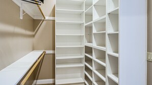 Ein begehbarer Kleiderschrank mit weißen Regalelementen und einer Holzbank.