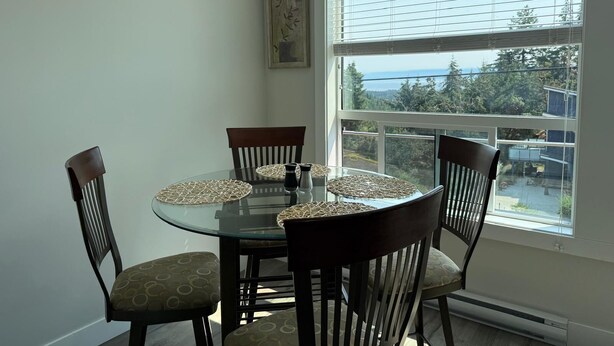 A dining area with a round glass table, four chairs, and a view of the outdoors through large windows.