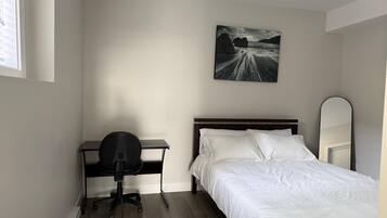A bedroom with a bed, a desk, a chair, a painting, and a mirror.