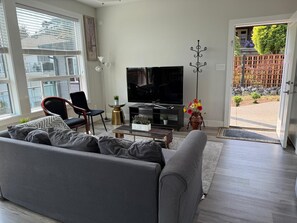 Un soggiorno moderno con un divano grigio, una poltrona nera, una TV a schermo piatto, un vaso decorativo con fiori e vista sull'esterno.