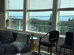 A room with large windows, a sofa, two chairs, and a small table with a plant.