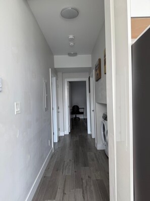 Un pasillo con lavadora y secadora, una puerta que da a una habitación y una lámpara en el techo.