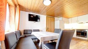 A dining area with a table and chairs, a television mounted on the wall, and a kitchen with cabinets and a stove. - Ferienwohnung Brügga (Brand)