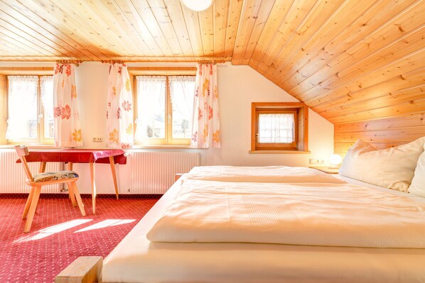 Een gezellige slaapkamer met houten plafond, een bed, een tafel met stoel en een raam met gordijnen.