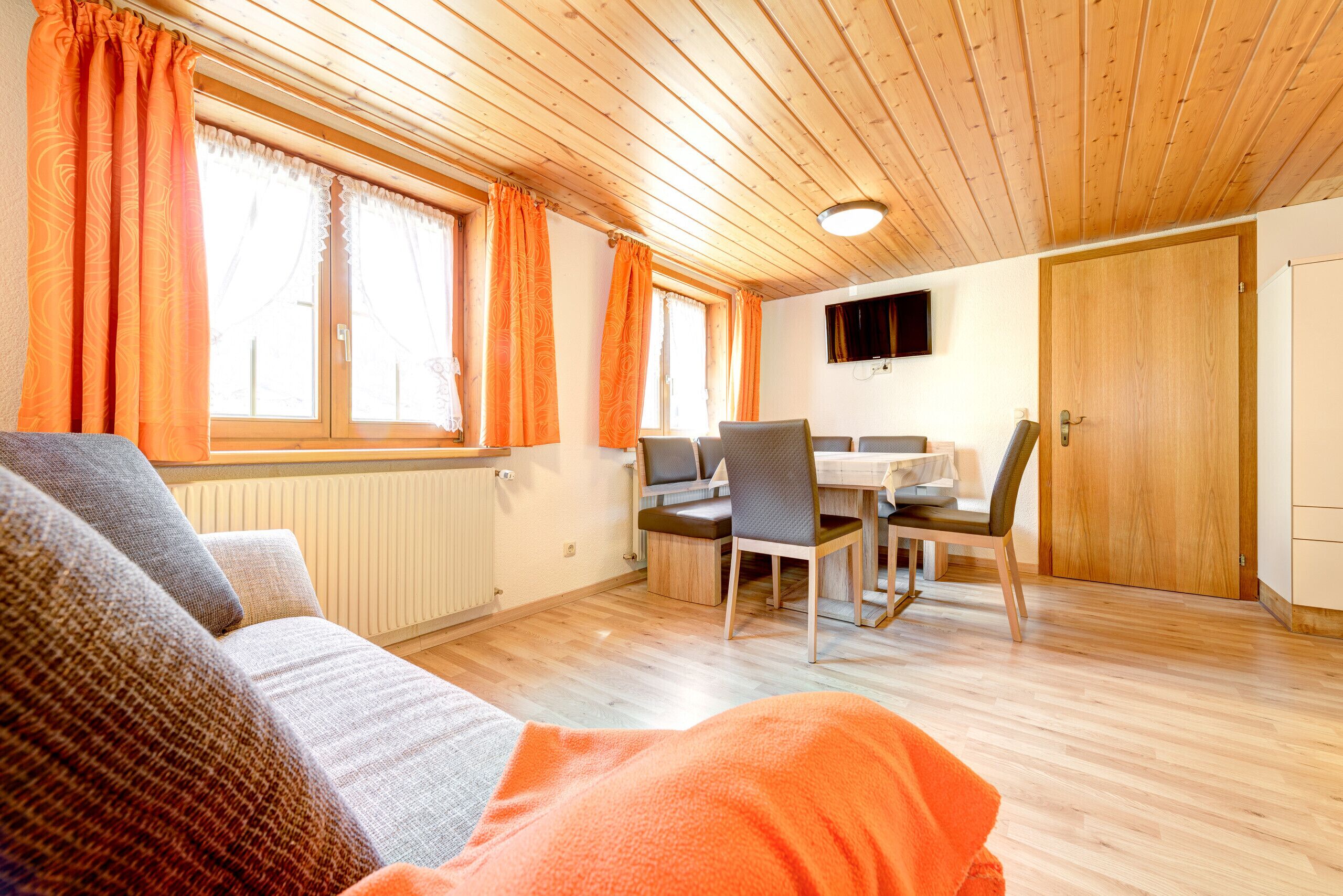Une pièce confortable avec un canapé, une table à manger et des chaises, un téléviseur et un plafond en bois.