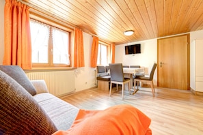 A cozy room with a sofa, a dining table with chairs, a television, and a wooden ceiling. - Ferienwohnung Brügga (Brand)