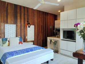A bedroom with a bed, a wooden wall, a brick-patterned wall, a ceiling fan, and a TV in the adjacent room. - Estudio 1 cama polo 15 (Playa del Carmen)