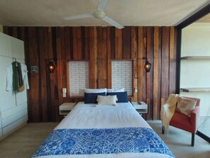 A bedroom with a large bed, wooden panel walls, a ceiling fan, and a red chair. - Habitacion con balcon (Playa del Carmen)