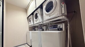 Uma área de lavanderia com duas máquinas de lavar e duas secadoras, um painel de controle e um micro-ondas fixado na parede.
