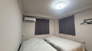 Quarto com duas camas, ar-condicionado e luminária no teto.