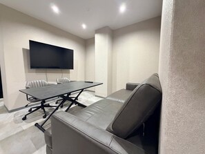 Een vergaderruimte met een grote tafel, meerdere stoelen, een bank en een flatscreen aan de muur.