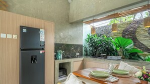 A modern kitchen with a built-in refrigerator, a dining table set for two, and a stone wall with plants. - Serene 2BR Retreat w Pool & Lounge, Canggu's Heart (Kuta Utara)