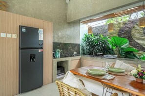 A modern kitchen with a built-in refrigerator, a dining table set for two, and a stone wall with plants. - Serene 2BR Retreat w Pool & Lounge, Canggu's Heart (Kuta Utara)
