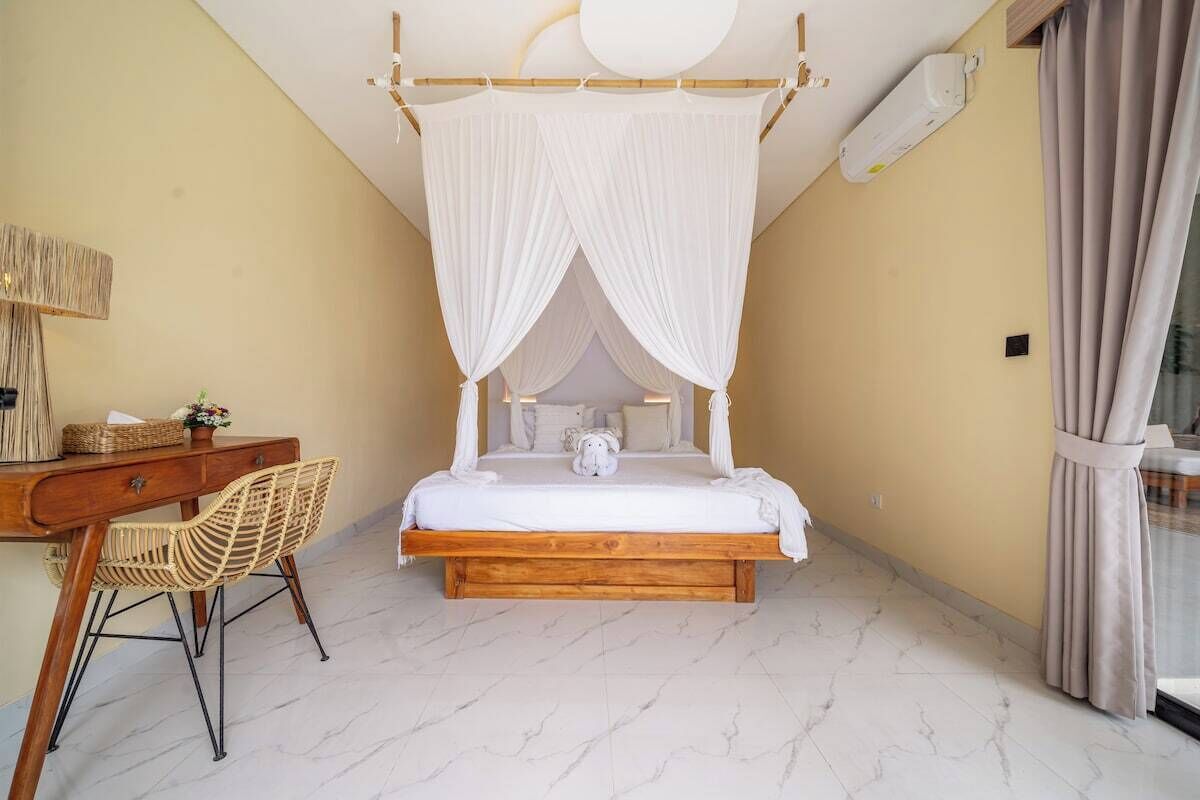 A bedroom with a four-poster bed, a wooden desk with a chair, and a bedside table.