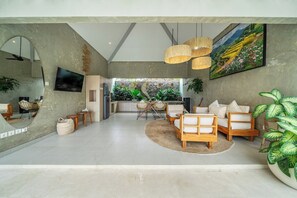 Una sala de estar moderna con un conjunto de sofás, un comedor con sillas, un televisor montado en la pared y una planta grande.