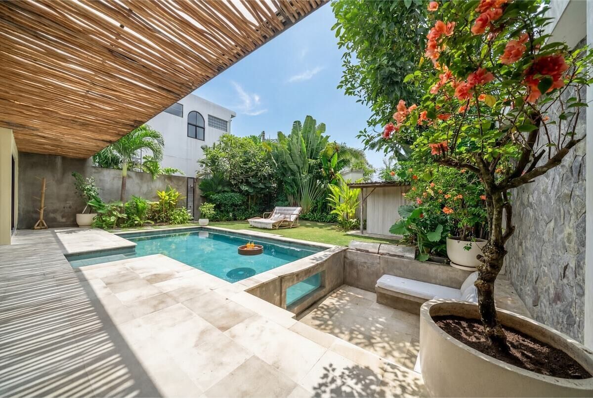 Piscina com pergolado de madeira, cercada por plantas em vasos e uma pequena área de estar.