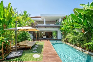 Ein modernes Haus mit Schwimmbad, umgeben von üppiger tropischer Vegetation.