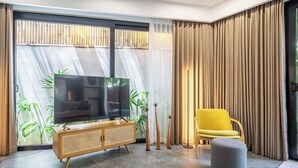 Uma sala de estar moderna com uma televisão, uma poltrona amarela e um banquinho cinzento.