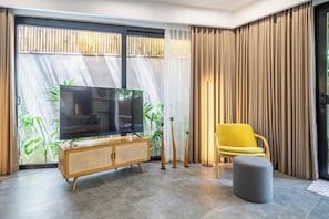 Ein modernes Wohnzimmer mit Fernseher, einem gelben Sessel und einem grauen Hocker.