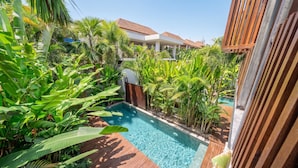 Piscina rodeada por vegetação tropical exuberante, com um deck de madeira e um edifício ao fundo.