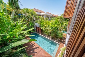 Ein Pool, umgeben von üppiger tropischer Vegetation, mit einer Holzterrasse und einem Gebäude im Hintergrund.