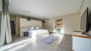 Quarto moderno com uma cama grande, uma televisão e uma parede de destaque em pedra.