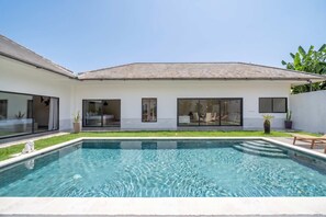 Ein modernes Haus mit Swimmingpool, großen Fenstern und einem gepflegten Rasen.