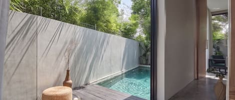 A modern interior with a pool, a wooden deck, and a view of greenery outside.