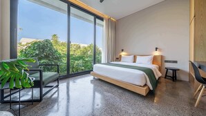 A modern hotel room with a large sliding glass door, a bed with a wooden headboard, a green plant, and a small table. - Chic 3BR Townhouse • Beach Nearby • Pool • Umalas (Kuta Utara)