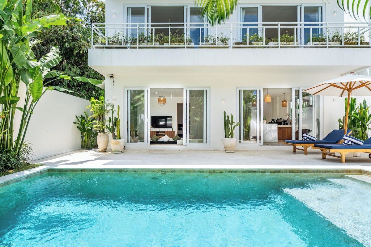 A modern two-story house with a swimming pool, outdoor seating, and lush greenery.