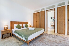 Ein Schlafzimmer mit einem großen Bett, einem Holzkopfende, Nachttischen und einem durch eine Tür sichtbaren Badezimmer.