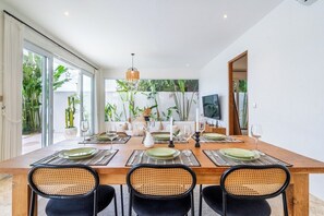 A dining area with a long wooden table set for four, surrounded by rattan chairs. - Tropical 3BR Canggu Stay w Pool, Balcony & Office (Kuta Utara)