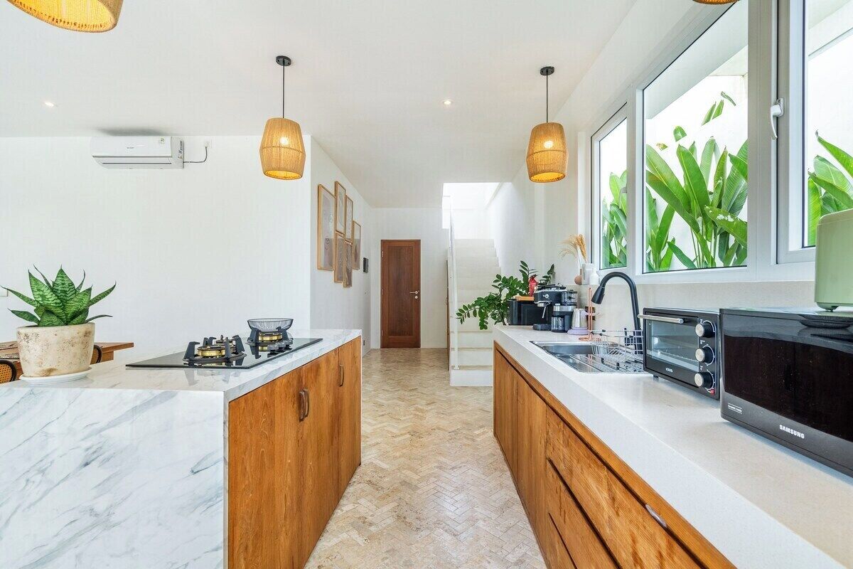 Een moderne keuken met een marmeren aanrechtblad, houten kastjes, een ingebouwde oven en een groot raam met planten.