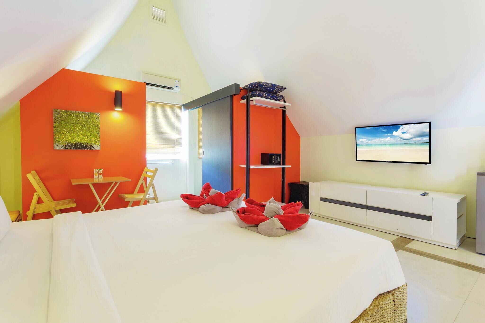 A bedroom with a bed, a desk, a chair, a TV, and a window.