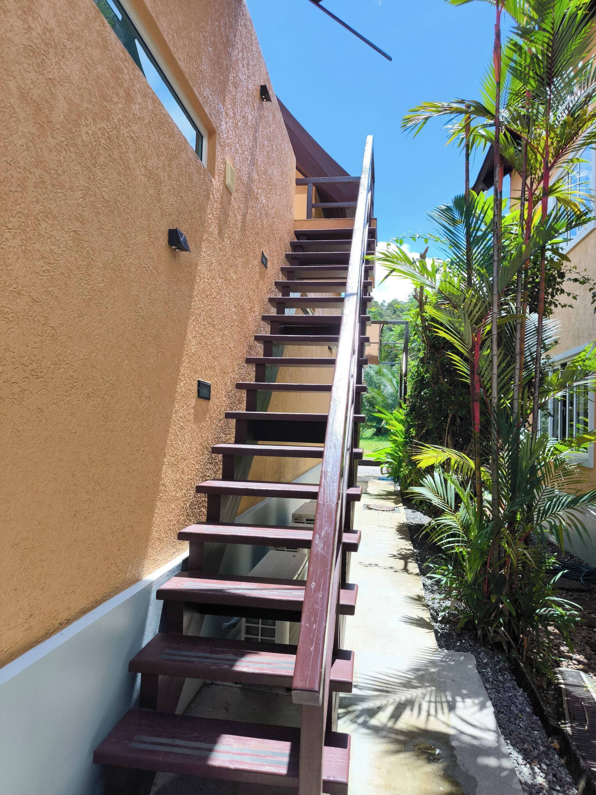 Eine Treppe führt zu einer oberen Etage, neben einem Gebäude mit einer strukturierten Wand und einem kleinen Fenster.