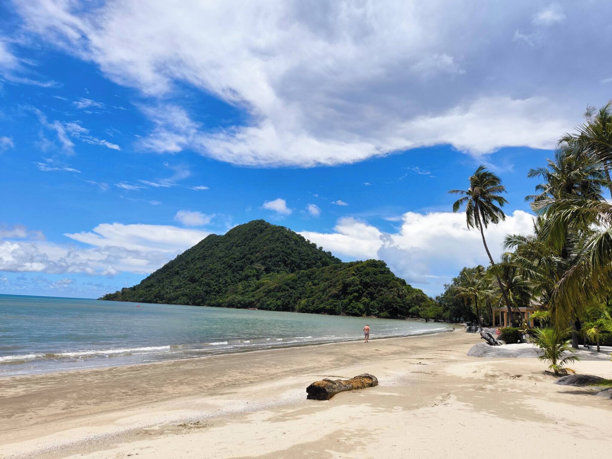 A beach with clear water, a sandy shore, and a mountain in the background.