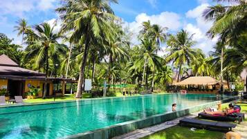 A pool area with lounge chairs and a thatched-roof structure.