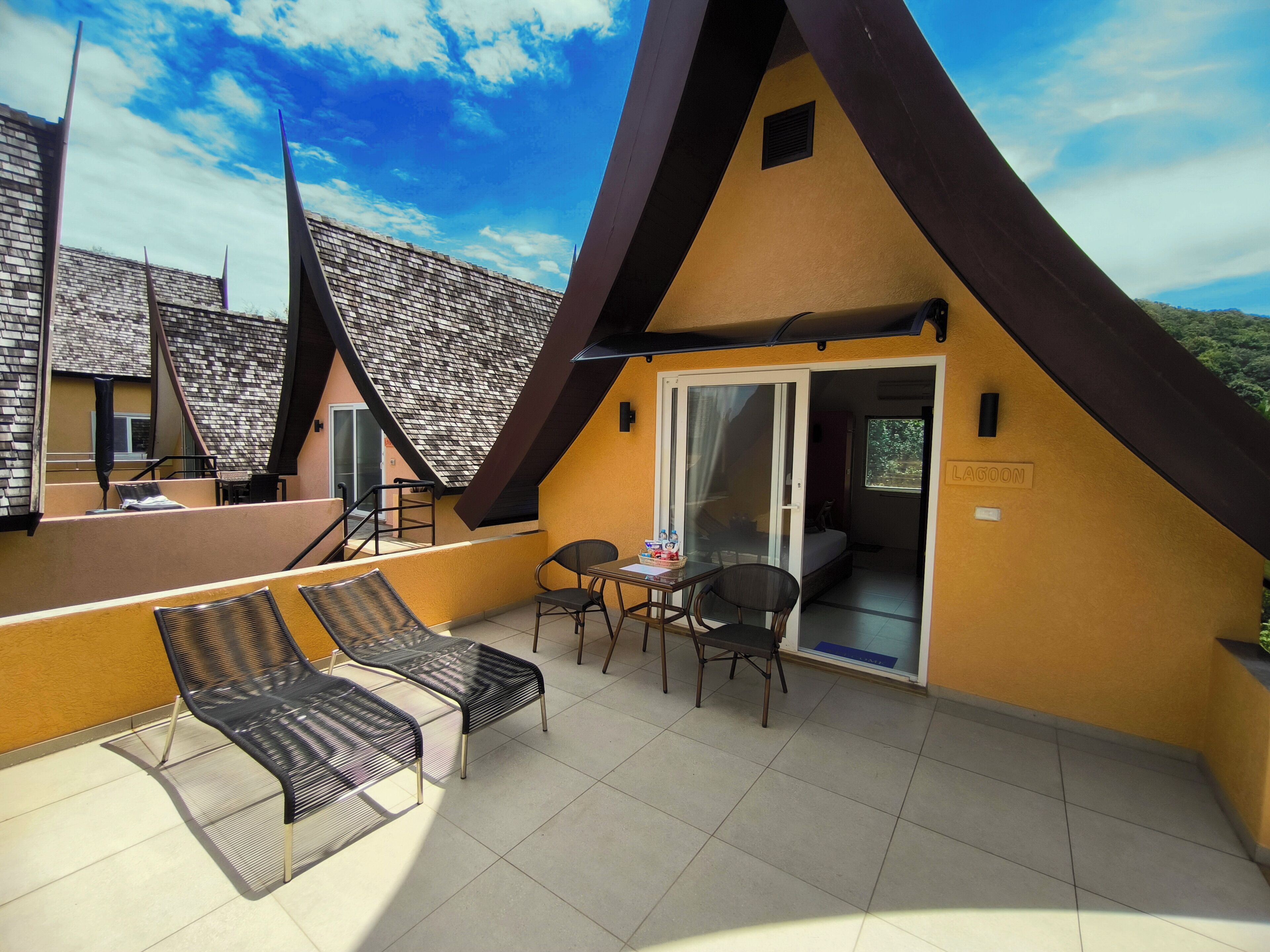A hotel room with a balcony, a bed, a table with chairs, and a view of the sky.