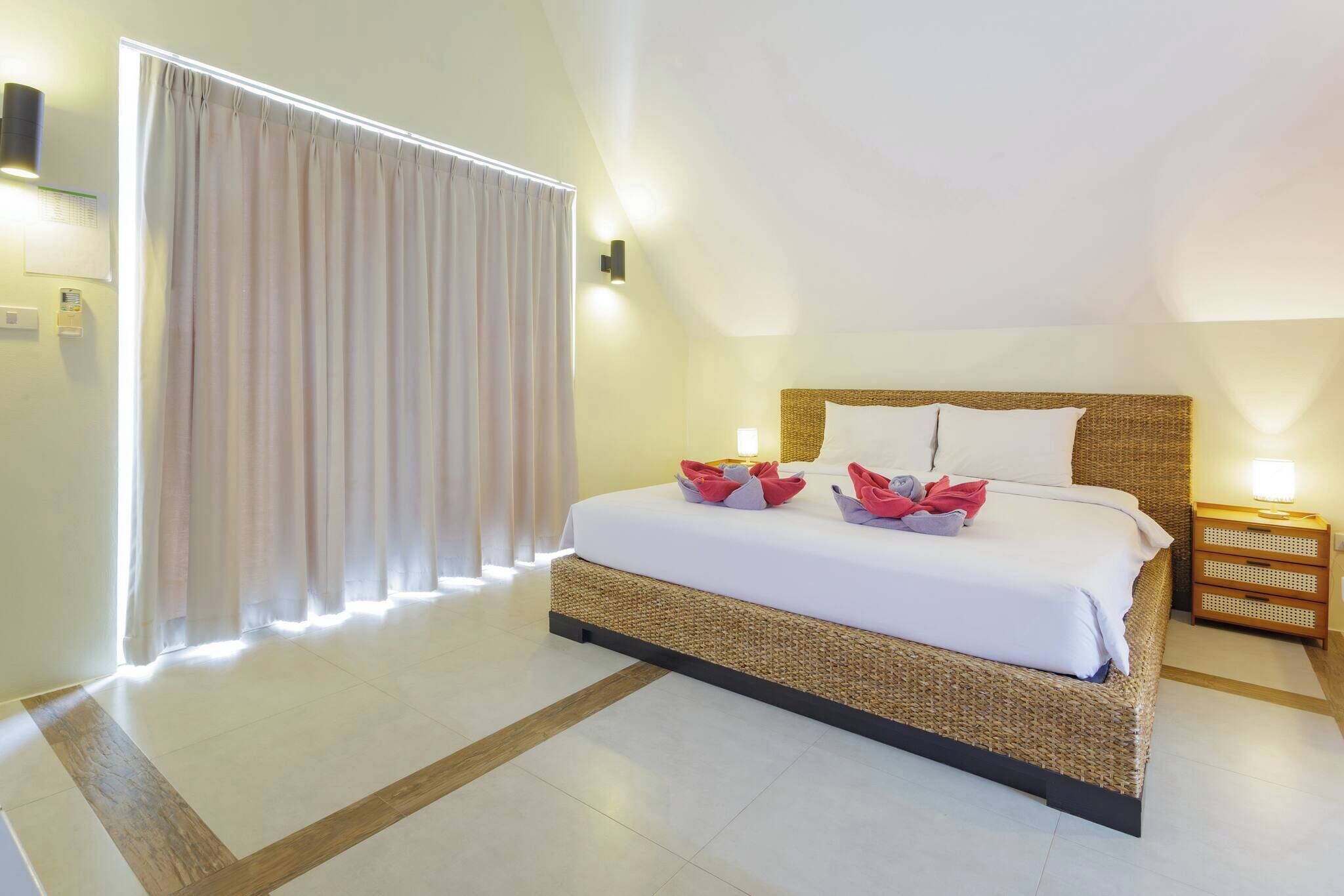 Une chambre d’hôtel avec un lit, une table de chevet, une lampe et une fenêtre avec des rideaux.