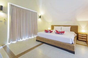 A hotel room with a bed, a nightstand, a lamp, and a window with curtains.