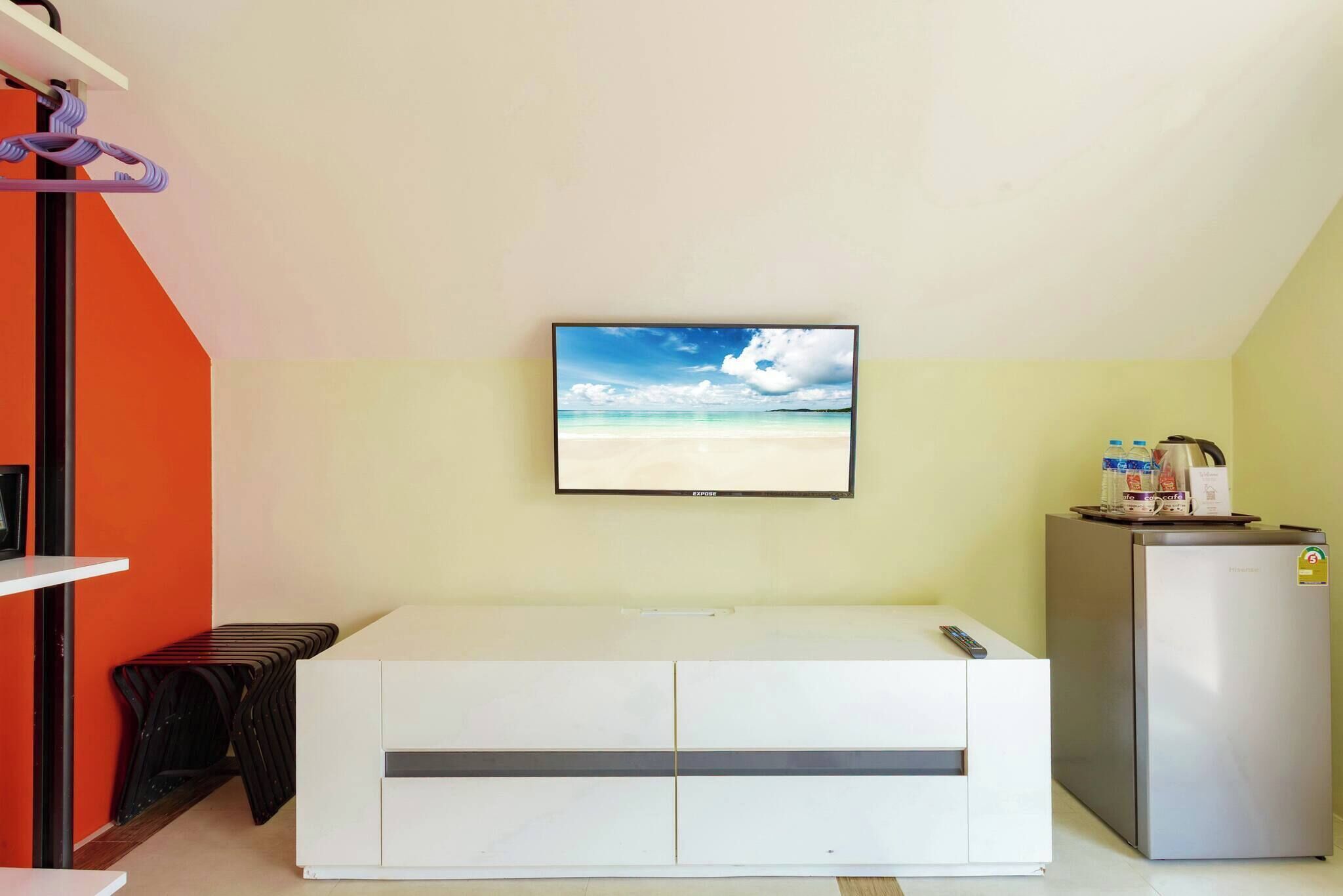A room with a bed, a television mounted on the wall, a refrigerator, and a small table with a remote control.