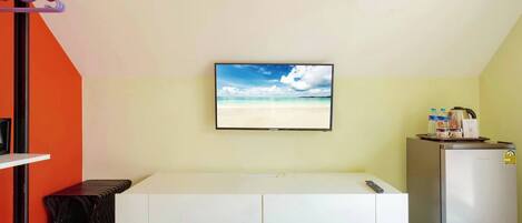 A room with a bed, a television mounted on the wall, a refrigerator, and a small table with a remote control.