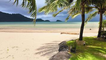 A beach with clear turquoise water, palm trees, and a large rock formation.