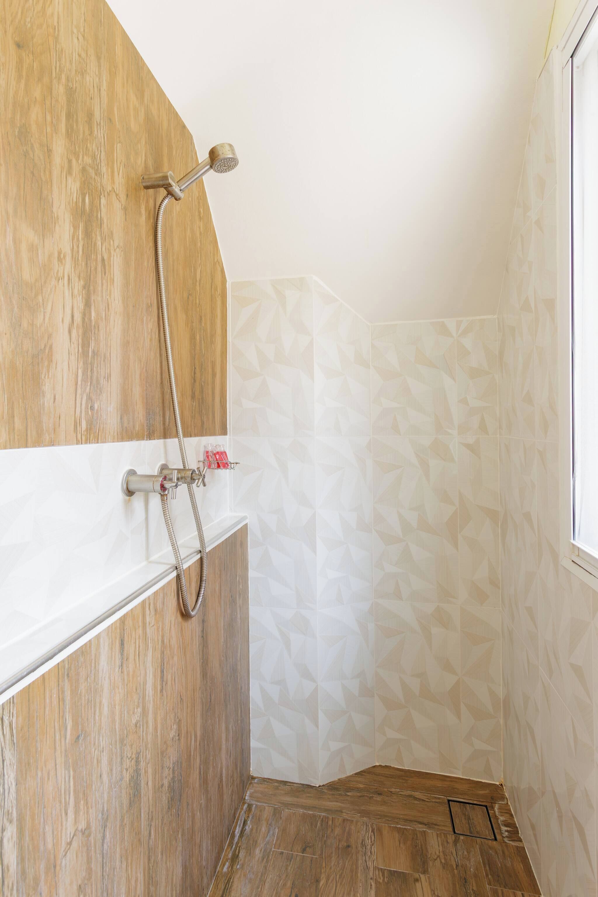 A shower with a wooden panel design, a white tiled wall with a geometric pattern, and a wooden floor.
